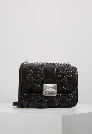 Schwarze, gesteppte Handtasche aus Leder, mit silbernen Nieten, einem Klappenverschluss mit einer metallischen Logo-Platte und einer Kettenriemen.