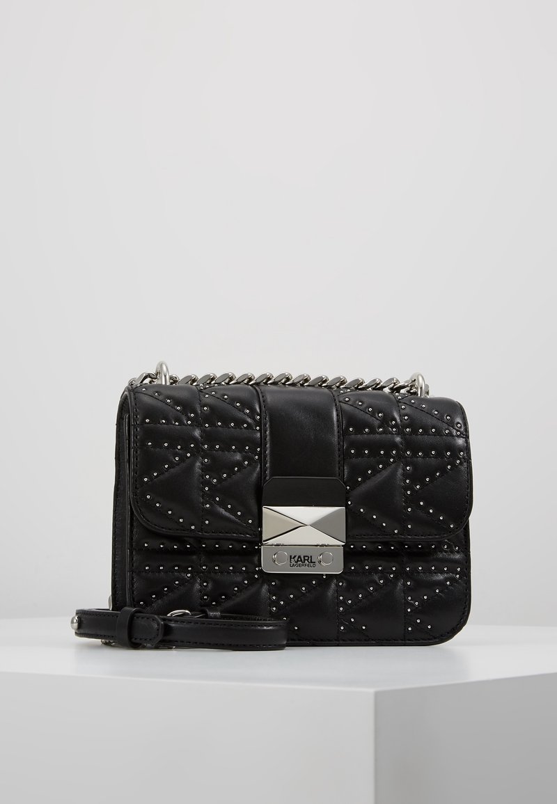 Borsa a tracolla nera trapuntata in pelle, caratterizzata da borchie argentate, chiusura a flap con placca logata metallica e tracolla a catena.