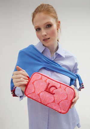 Bolso de mano de color rojo con un diseño de hojas de palma, textura suave y un logo prominente. El bolso tiene una cremallera y un ribete en contraste.