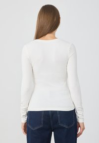 Top bianco a maniche lunghe con scollatura rotonda, vestibilità slim e texture a costine. Abbinato a jeans blu a vita alta con tasche posteriori.