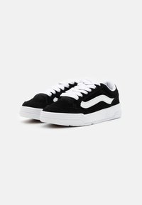 Schwarze Wildledersneaker mit weißen Schnürsenkeln und seitlichem Streifen. Dicke weiße Gummisohle; niedrige Bauweise mit strukturiertem Obermaterial und verstärkter Zehenkappe.