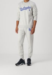 Felpa grigia chiara e pantaloni della tuta abbinati con grafica blu "Los Angeles". Il tessuto sembra morbido con polsini e vita a costine.