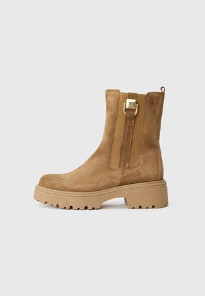 Tanfarbene Wildleder-Stiefelette mit einer massiven Gummisohle, seitlichen elastischen Einsätzen, einer Schlaufe hinten und einem goldenen quadratischen Schnallenakzent.