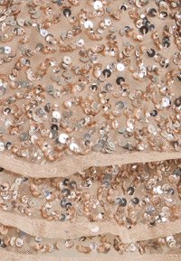 Tissu à sequins de couleur pêche clair, présentant de nombreux petits sequins circulaires argentés sur une base en maille, superposés en sections froncées.