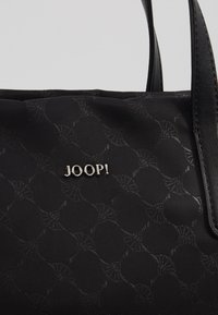 Schwarze Handtasche mit strukturierter Oberfläche, Lederakzenten und einem metallischen Logo. Robuste Griffe runden das Design ab.