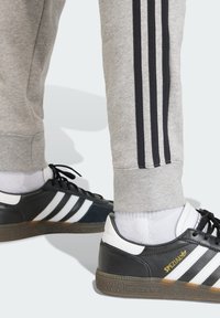 Crno-bijele sportske tenisice s teksturiranim gumenim potplatom, uparene s sivim trenirkama koje imaju crne pruge uz bočne strane.