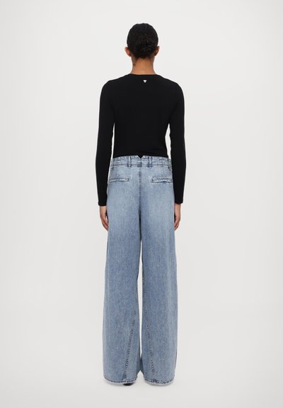 Black long-sleeve top and light blue wide-leg jeans. Denim has a faded finish, with back pockets on the jeans and a small logo on the top.