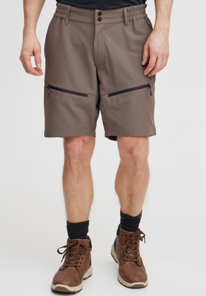 Brune shorts med elastisk talje, to lynlåsede frontlommer og lige pasform. Bæret med brune vandrestøvler og marineblå strømper.