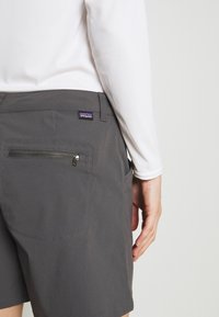 Harmaat shortsit, jotka on valmistettu kevyestä materiaalista. Niissä on vetoketjullinen tasku, näkyvät ompeluyksityiskohdat ja Patagonia-logo vyötärön lähellä.