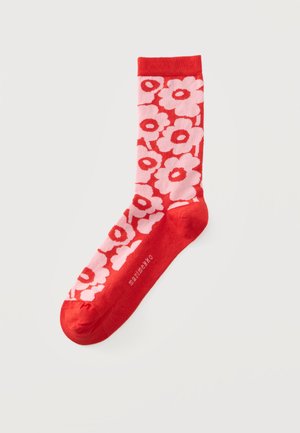 Червен чорап с ярък розов цветен мотив и думата "marimekko", отпечатана близо до пръстите, на светлосив фон.