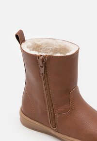 Bottine en faux cuir marron avec une fermeture éclair sur le côté, doublure beige douce et surface extérieure texturée. Bout rond et semelle en caoutchouc minimaliste.