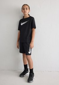 Conjunto atlético negro de Nike que incluye una camiseta de manga corta y pantalones cortos, con un acento de logo blanco en ambos. Zapatillas negras con detalles blancos.