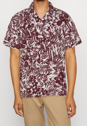 Camicia da uomo a maniche corte con bottoni, con motivi floreali e foglie bordeaux su sfondo chiaro, indossata con pantaloni beige.