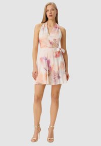 Abito a stampa floreale con scollo all'americana in colori pastello chiari, caratterizzato da un design incrociato, dettaglio con cintura annodata in vita e gonna svasata con pieghe. Sandali con cinturino alla caviglia dorati.