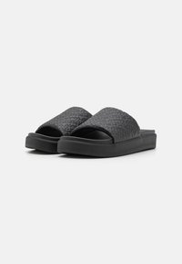 Sorte sliders med tekstureret mønster på overdelen, polstrede såler og åben tå-design. Det glatte materiale giver et elegant udseende.
