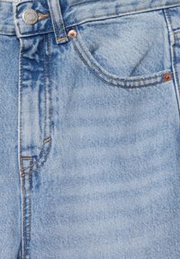 Jeans de mezclilla azul claro en primer plano que muestran el bolsillo frontal, el lazo del cinturón, el botón y detalles de costura naranja.