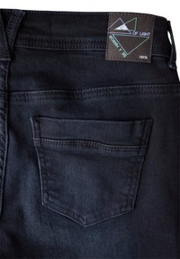 Mörka denimjeans med en liten bakficka, sydda linjer och en brun etikett med en geometrisk design och text.