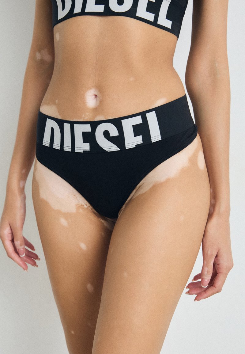 Svart bikini-sett med bredt midjebånd med "DIESEL"-logo i hvitt. Stoffet er glatt med en tettsittende design og minimal dekning.
