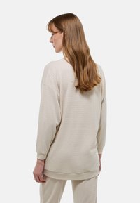 Pull en tricot beige clair à coupe décontractée, manches longues et motif texturé. Il présente un col rond et des poignets côtelés.