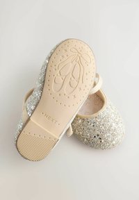 Lapse sädelev kuldne Mary Jane king, mille kummist põhi on kaunistatud embosis olevate balletikingade ja tähe mustriga, ning rihm üle toe.