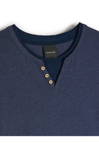 Granatowa koszulka z dekoltem w serek, z trzema drewnianymi guzikami i gładką fakturą. Metka widoczna wewnątrz kołnierza.