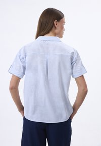 Camicia a maniche corte a righe blu e bianche con spacco sul retro, orlo arrotondato e maniche arrotolate, realizzata in tessuto leggero.
