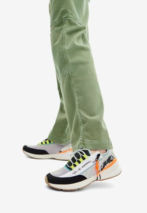 Baskets multicolores avec une tige en maille et des accents noirs, des lacets verts, des détails orange et une semelle texturée, associées à un pantalon cargo vert clair.