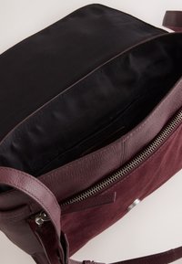 Bordeauxrode tas met leer- en suède texturen, voorzien van een ritssluiting, interieur gevoerd met zwarte stof en een afneembare riem.