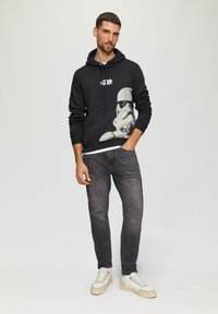 Czarna bluza z kapturem z grafiką Stormtroopera i białym napisem "Star Wars", zestawiona z przetartymi ciemnymi dżinsami i jasnymi trampkami.