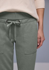 Jasnozielone, teksturowane spodnie dresowe z troczkiem w pasie i dwoma przednimi kieszeniami, zestawione z jasnobeżowym swetrem.