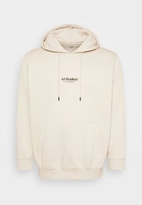 Cremefarbene Kapuzenjacke mit Kordelzügen, Fronttasche und bedrucktem "JJ Studios"-Logo. Ausgestattet mit gerippten Bündchen und Saum. Weiches Material mit glatter Textur.