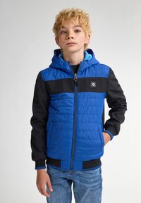 Giacca con cappuccio blu e nera, con texture trapuntata, chiusura con zip, accenti a contrasto e polsini a coste. Indossata da un bambino su uno sfondo neutro.