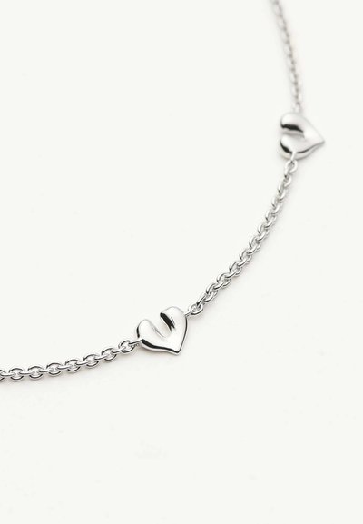 Ασημένιο βραχιόλι με αλυσίδα που διαθέτει δύο μικρά, γυαλιστερά γοητευτικά καρδιάς διακοσμητικά, τοποθετημένα ομοιόμορφα ανάμεσα στους κρίκους, πάνω σε λευκό φόντο.