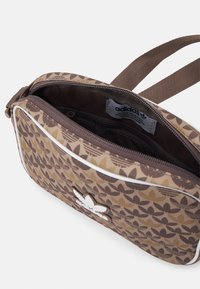 Brączowy torebka przerzucana z wzorem i białymi akcentami oraz logo. Posiada jedną główną kieszeń na zamek oraz wnętrze z dodatkową kieszonką dla lepszej organizacji.