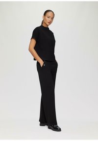 T-shirt nero con una vestibilità ampia e un collo alto abbinato a pantaloni neri a gamba larga. L'outfit presenta sottili dettagli metallici e una texture liscia.