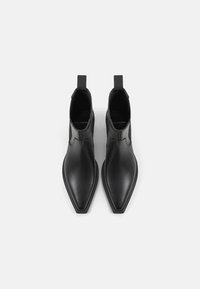 Bottines noires en cuir lisse avec un bout pointu et un design minimal. Elles sont dotées de panneaux élastiques sur les côtés et de languettes de traction.
