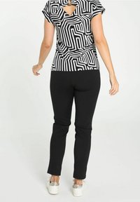 Top negro de mangas cortas con un patrón geométrico blanco, detalle de espalda descubierta, combinado con pantalones negros ajustados y zapatos blancos con acentos de purpurina.