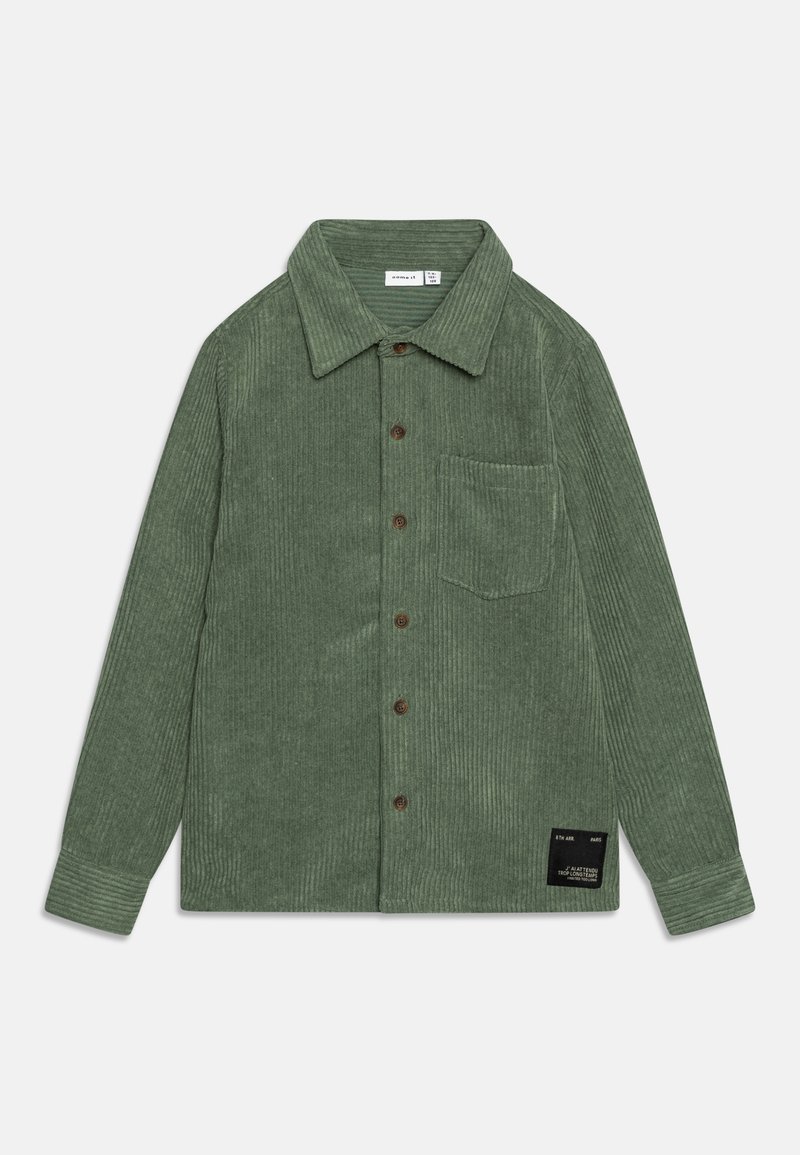 Chemise en velours côtelé vert à manches longues, avec boutons sur le devant et une poche poitrine. Caractérisée par une surface texturée et une étiquette de marque près de l'ourlet.