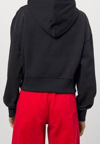 Avklippt svart hoodie med huva, ribbat nederkant och vida ärmar, tillsammans med röda vida byxor med bakfickor.