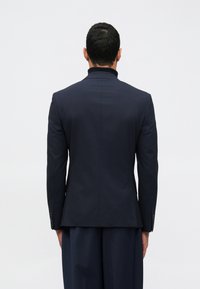 Ναυτικό σακάκι προσαρμοσμένο με ψηλό γιακά, δομημένους ώμους και κομψή εφαρμογή. Διαθέτει διακριτική ραφή και δύο κουμπιά.