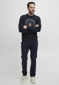 Námořnická modrá mikina s designem loga, žebrované manžety a lem; spárované s odpovídajícími námořnickými kalhotami a bílými teniskami. Jednoduchý a ležérní střih.