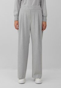 Pantalons larges gris clair avec une taille texturée, en tissu doux et avec des plis pour une coupe décontractée. Portés avec des baskets blanches.