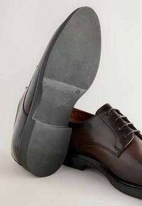 Braunes Leder Schuh mit glatter Oberfläche, runde Spitze und klassischen Schnürsenkeln. Schwarze Gummisohle mit strukturiertem, geriffelten Design.