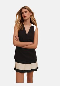Top negru fără mâneci cu un design în V, asociat cu un skort plisat care are dungi alternante negre și crem. Textura materialului este netedă.