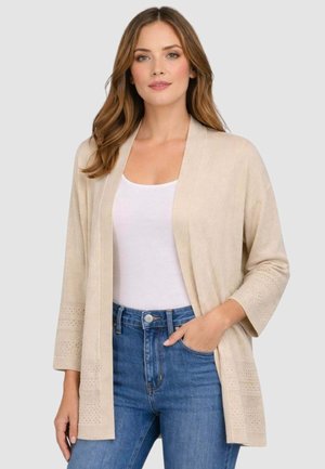 Cardigan beige con maniche a tre quarti, apertura frontale e dettagli testurizzati sull'orlo delle maniche. Indossato sopra una maglia bianca e jeans a vita alta.