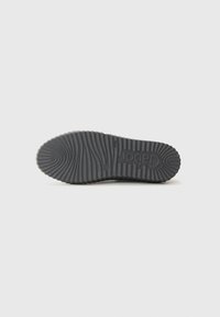 Suola di scarpa in gomma nera con un motivo testurizzato e rigato e un logo. Presenta una forma arrotondata e un profilo piatto per stabilità.