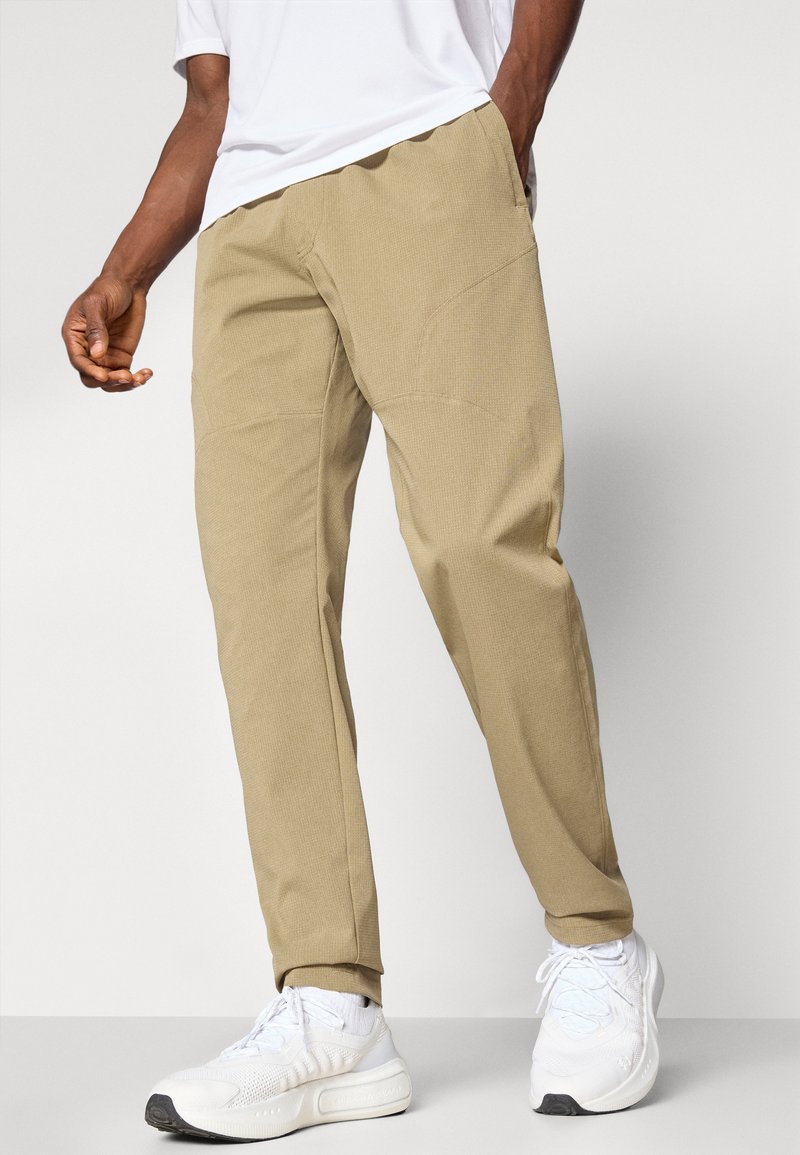 Beige Hosen mit entspannter Passform, ausgestattet mit strukturiertem Stoff, Seitentaschen und schmalem Nähen. Kombiniert mit weißen Sportschuhen.