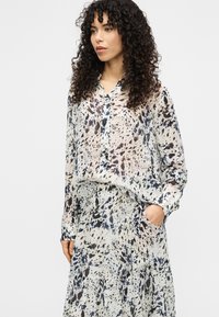 Μπλούζα με κουμπιά και ταιριαστή φούστα από ελαφρύ, ημιδιαφανές ύφασμα με μοτίβο πιτσιλιών σε αποχρώσεις του μπλε, κρεμ και καφέ.