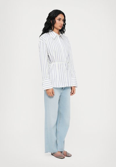 Camicia a maniche lunghe bianca a righe con ampi polsini e vita cintata, abbinata a jeans a gamba larga di un blu chiaro e ballerine a righe multicolori.