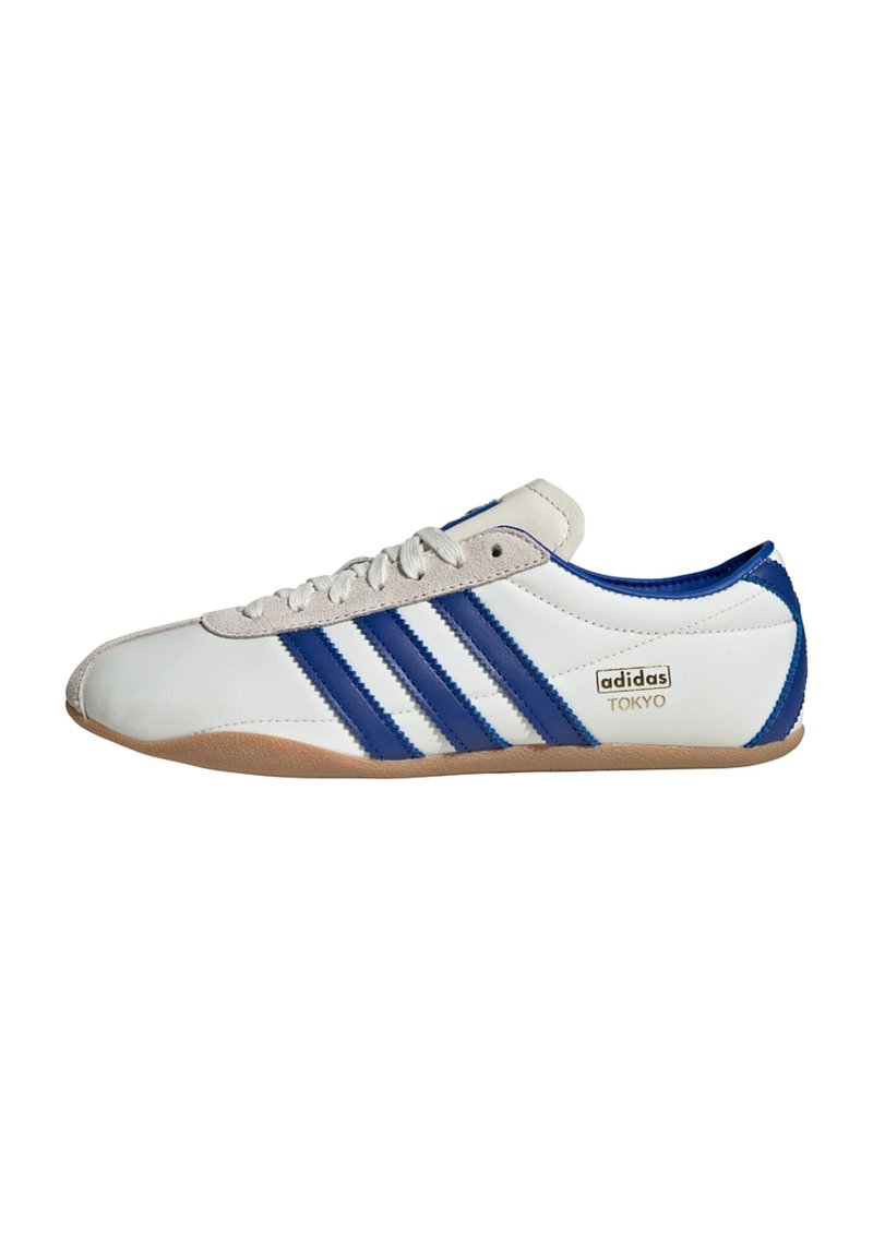 Vit sportskänga med blå accenter, som har tre ränder, en mockatå och en gummisula. Texten lyder "adidas TOKYO."